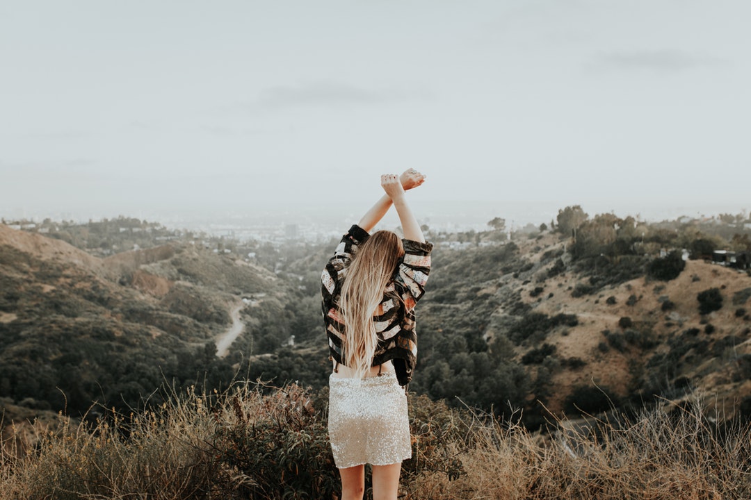 A woman holding her arms up in the sky on top of a mountain.