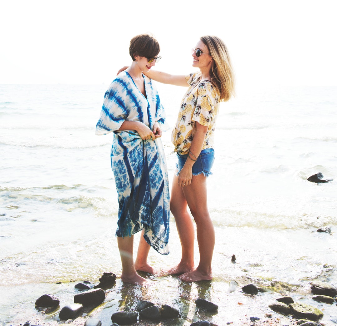 woman with her right hand on shoulder of another woman standing on beach