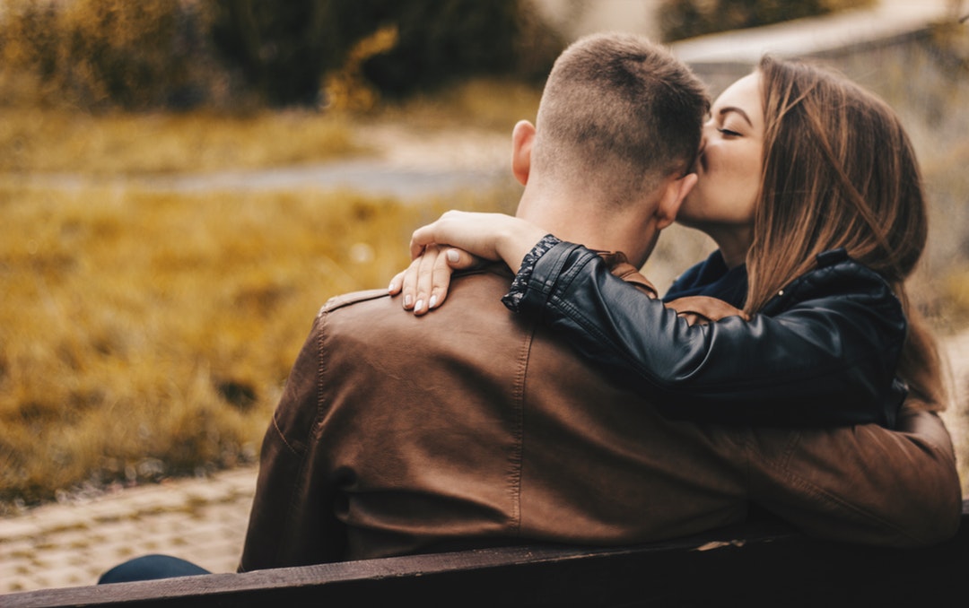 woman kissing man on head while sitting on bench