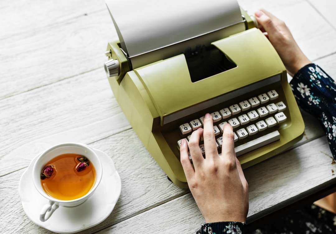 flat-lay photography of person using typewriter beside cup of tea