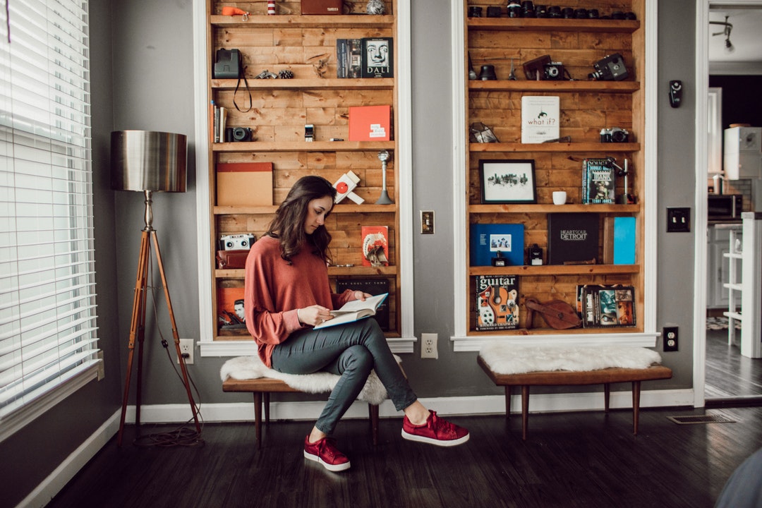 woman reading books sitting on brown ottoman chair