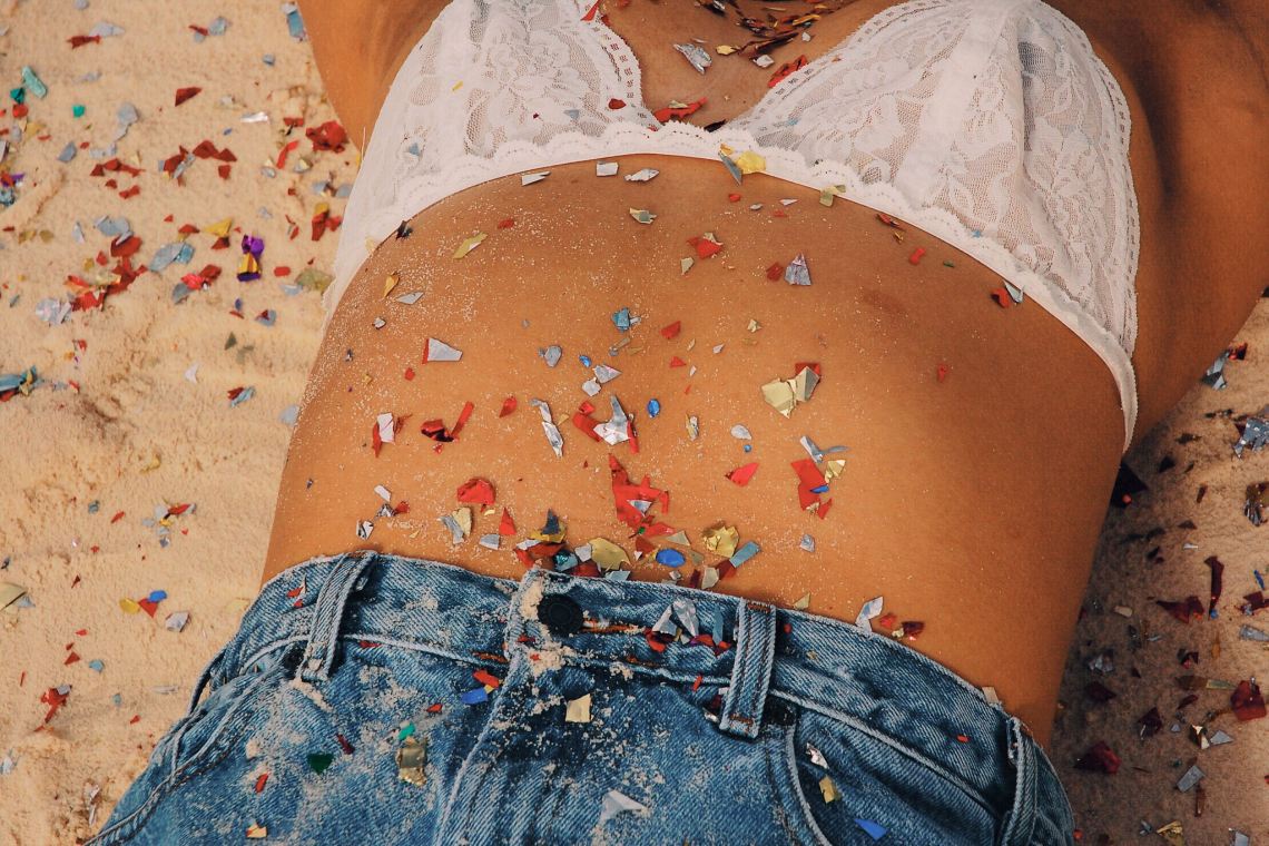 girl with white bra and jean shorts laying on sand with glitter on her