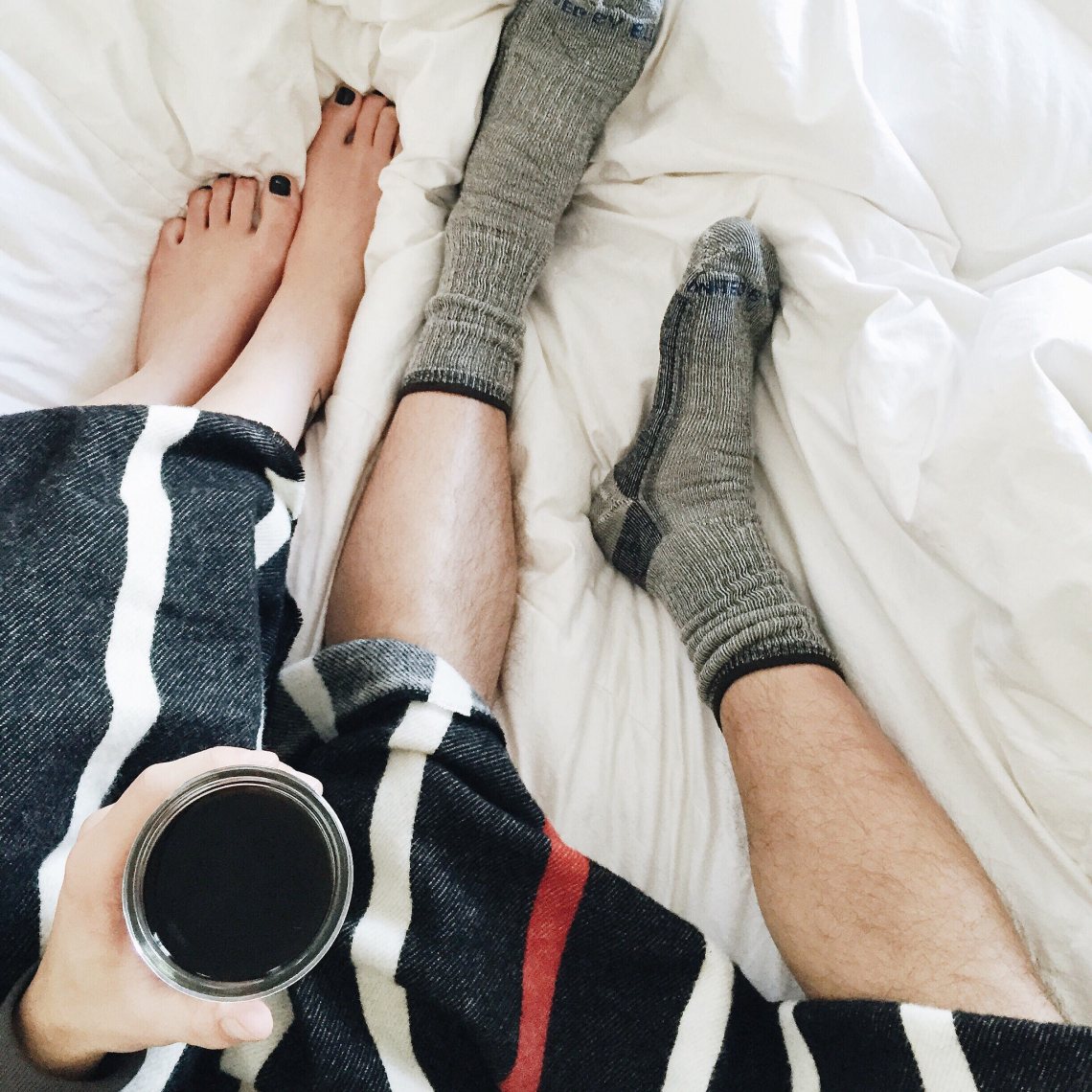 couple in bed tangled sheets with coffee and a blanket