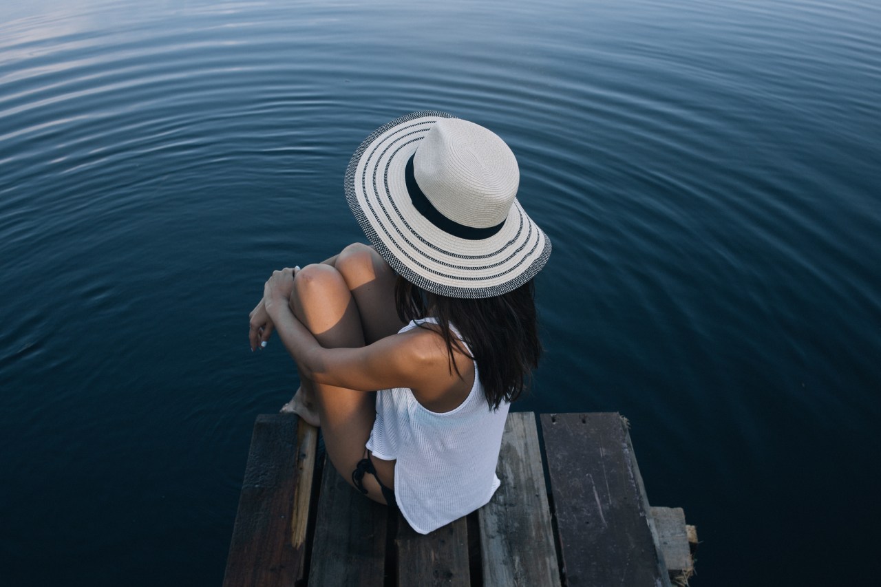 Woman sits on a doc, staring out at the water