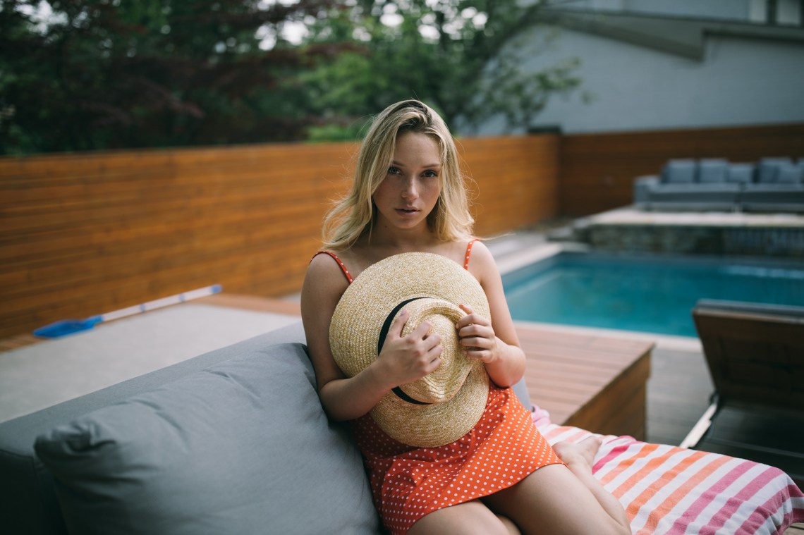 girl in a red dress by a pool with a sun hat