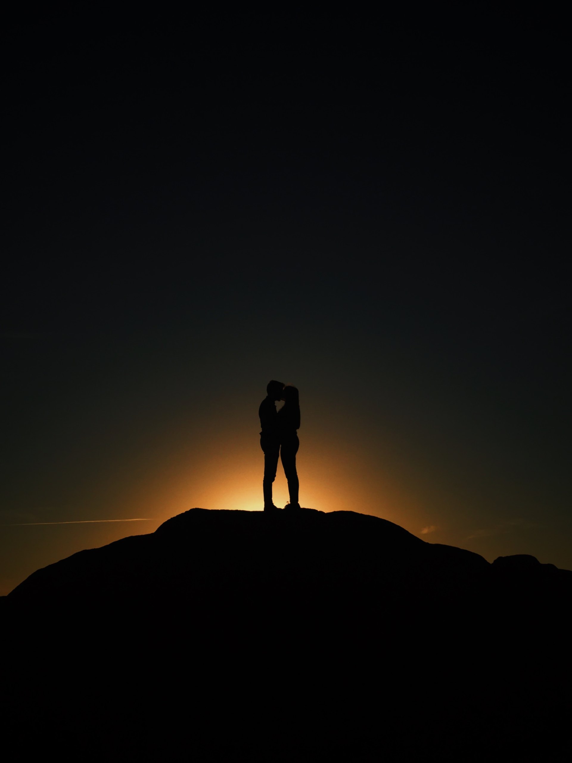 Man and woman stand in the dark on the horizon holding each other close