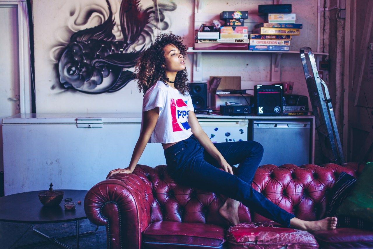 Young woman in Pepsi cropped tee t-shirt sitting on red leather couch, vintage board games