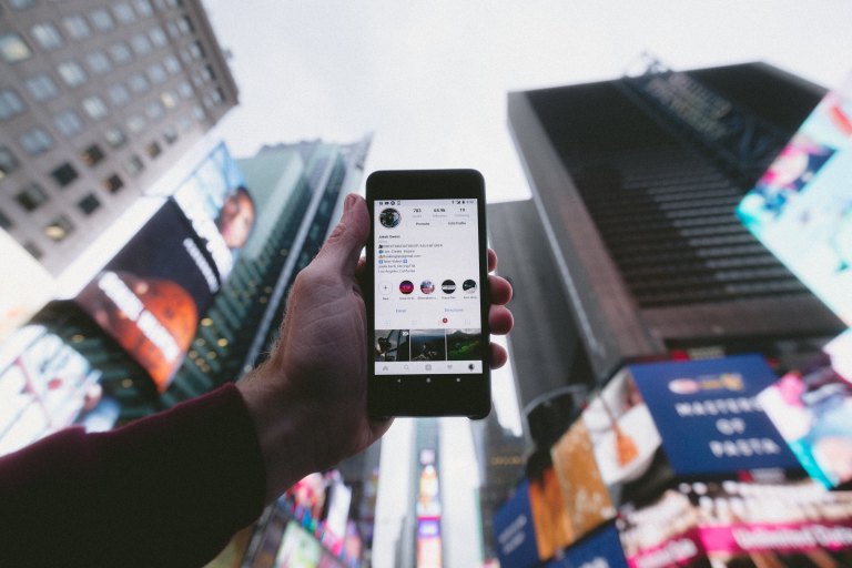 A man holding up his phone on Instagram in a city