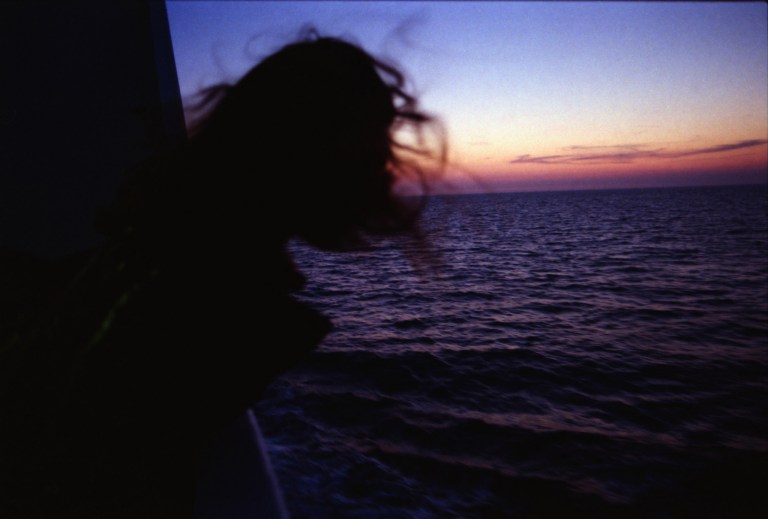 Girl on a boat leaning out to watch the sunset