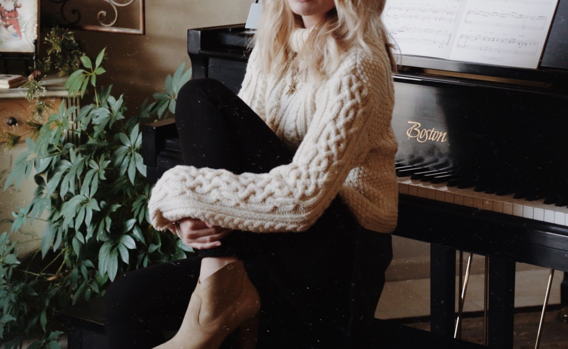 woman sitting in comfy sweater in front of piano