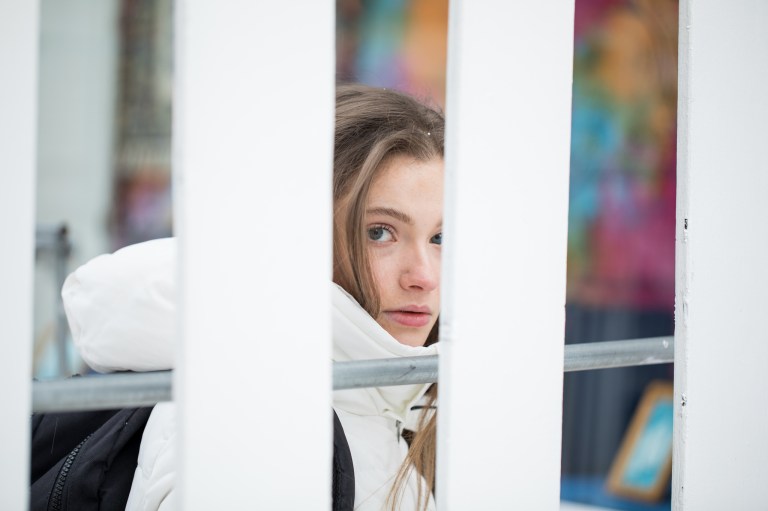 Girl in a white coat looking back from behind the fence