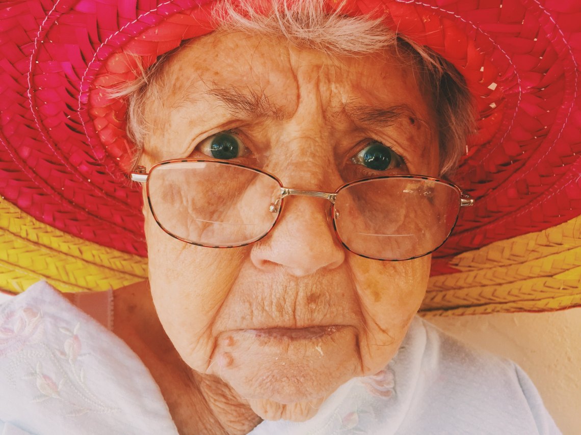 A grandma stares into the Camera with her glasses and red hat