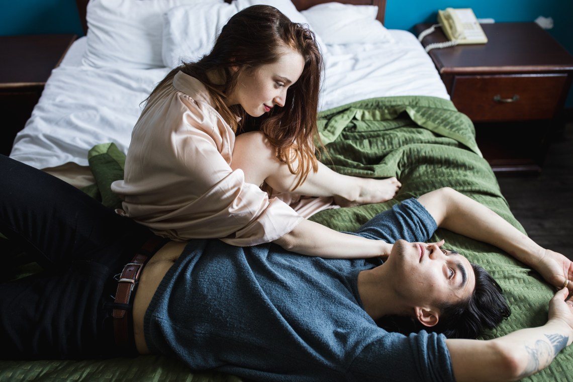 couple sitting on green bed staring at each other