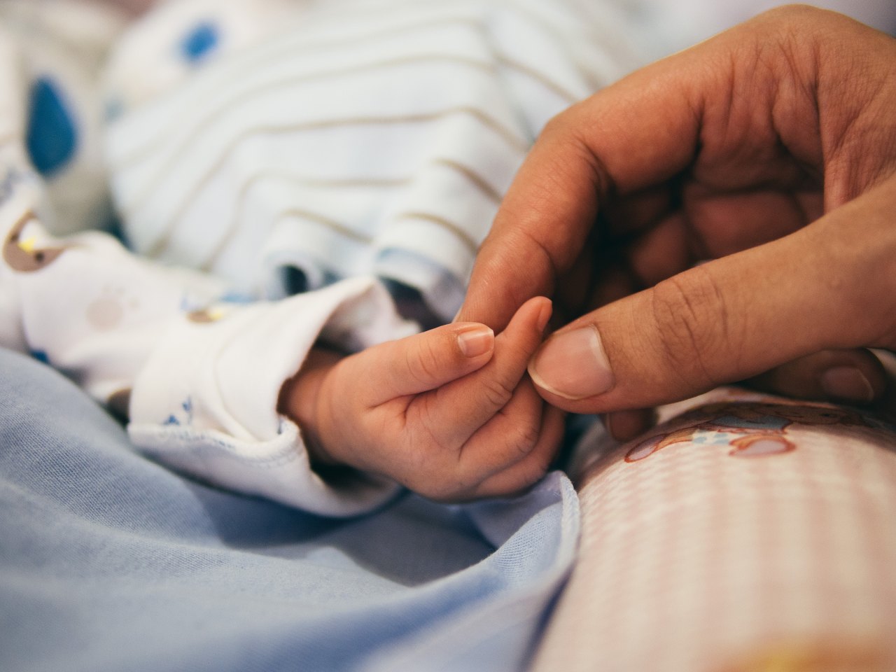 A baby and his parent hold hands