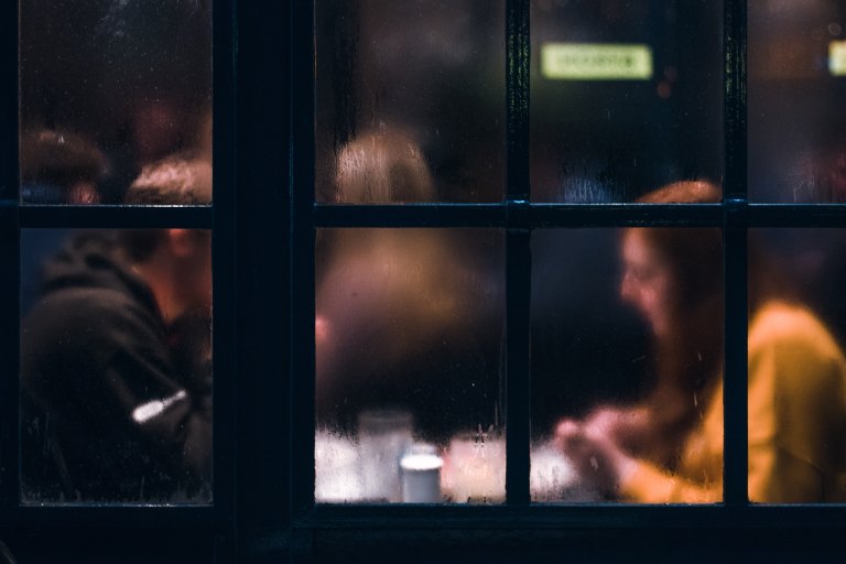 A man and a woman sit at a table, blurry through a window