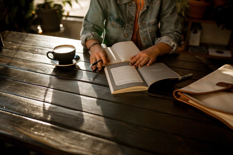 a writer sits at a table with coffee and her notebook