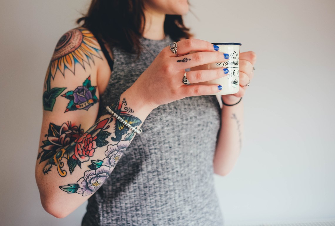 woman with tattoos holding coffee cup