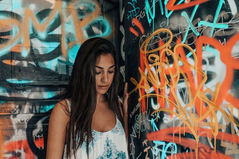 woman in white and blue tank top standing beside graffiti wall