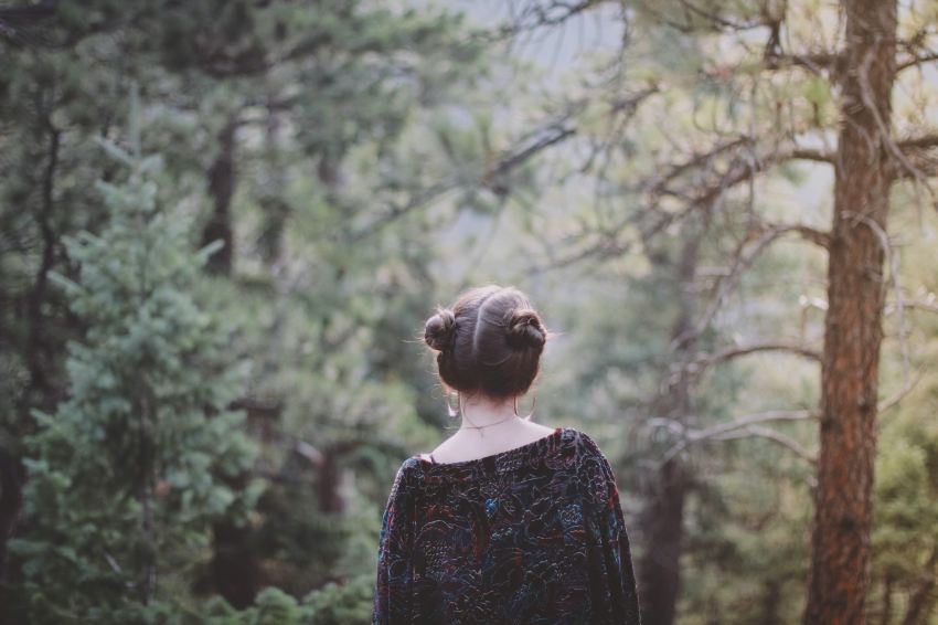 woman standing facing green forest