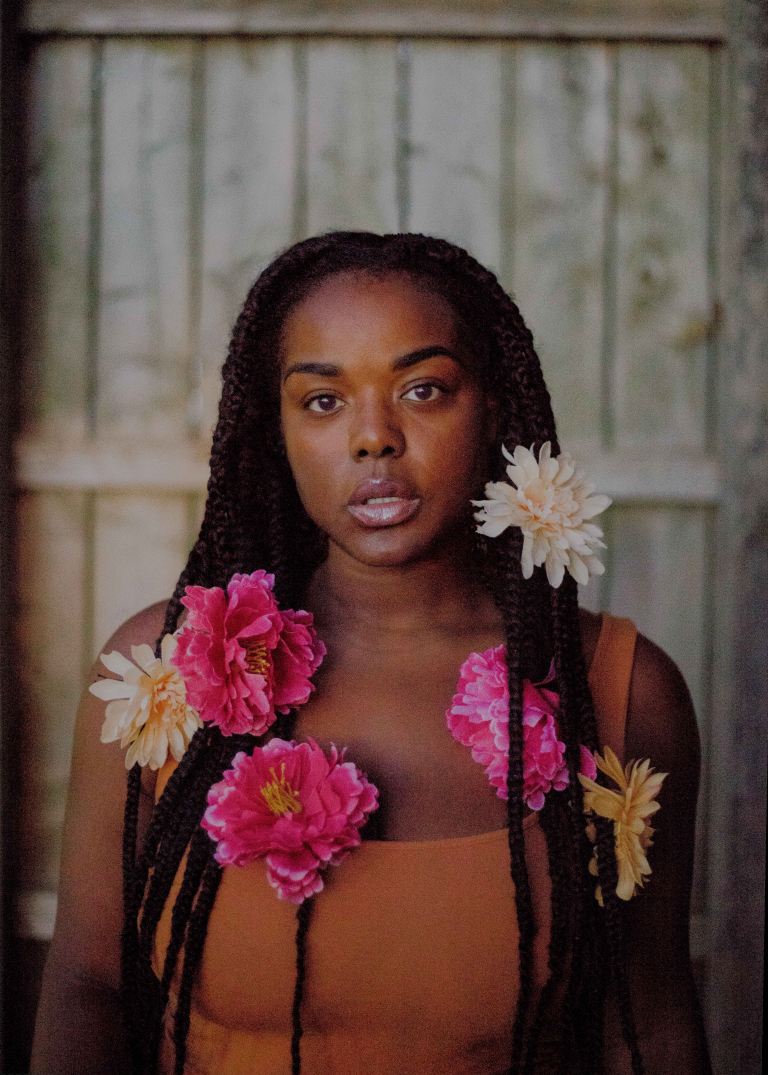 woman standing near white wall with multicolored flowers on her hair