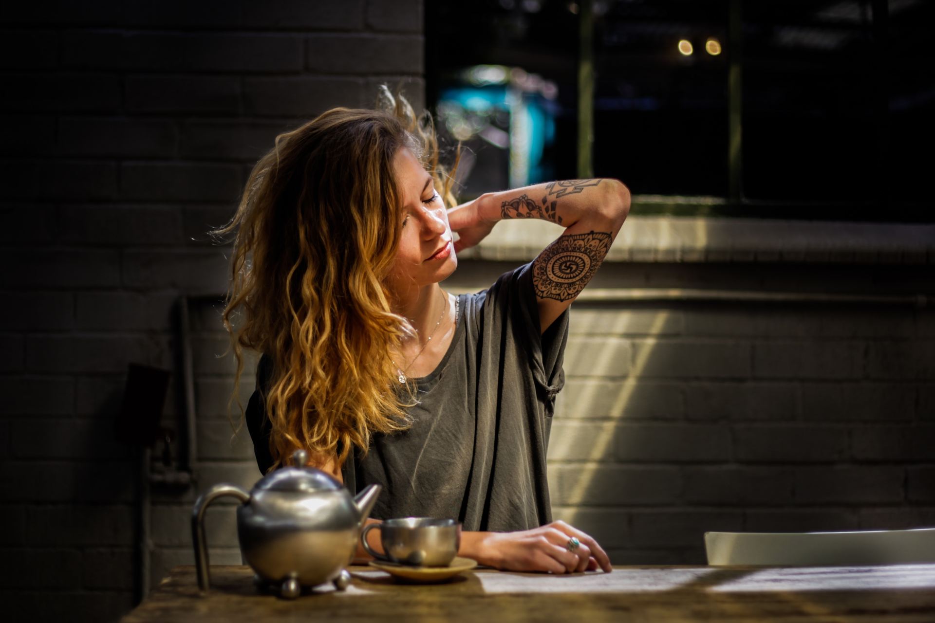 woman in gray top sitting beside gray tea pot and cup on brown wooden table