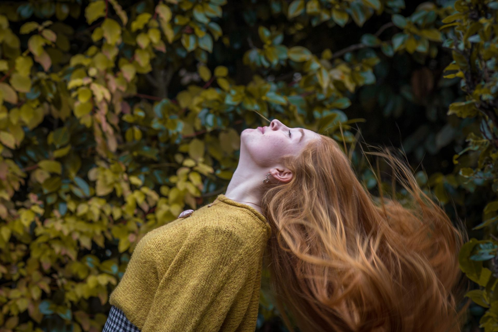 woman wearing brown crew-neck shirt standing in front of green leaves