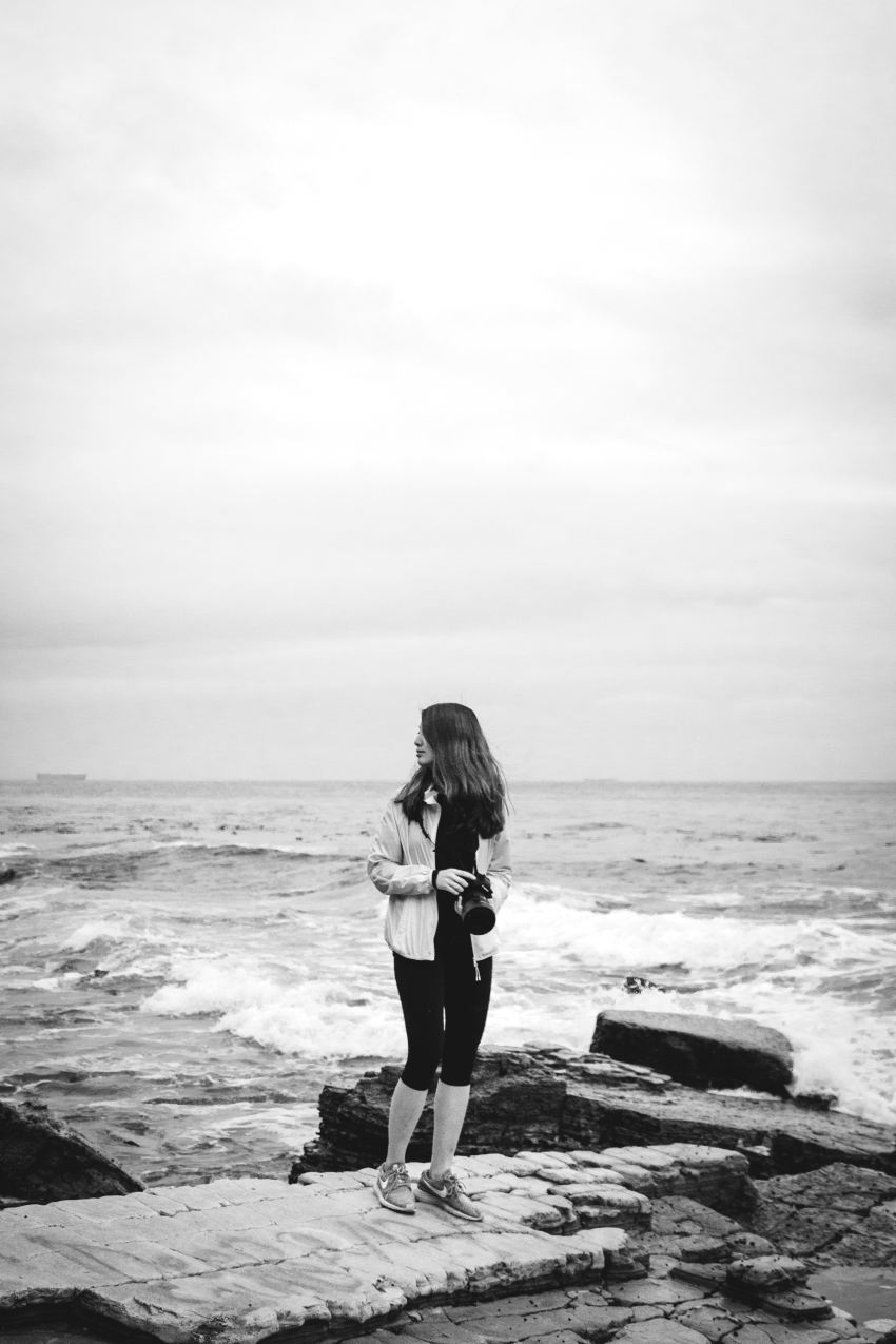 grayscale photography of woman holding camera by sea