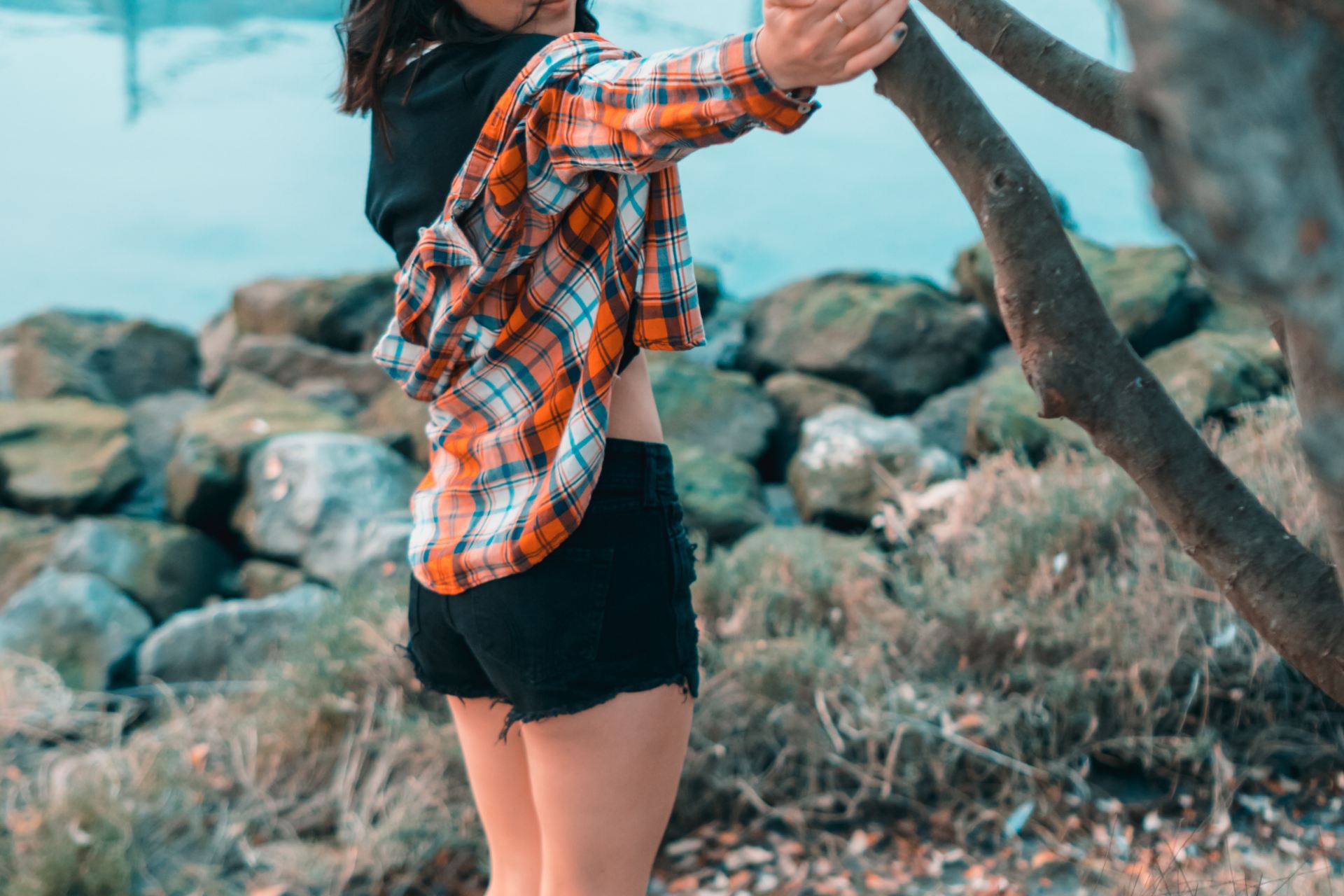 woman wearing orange plaid blouse standing beside tree near body of water