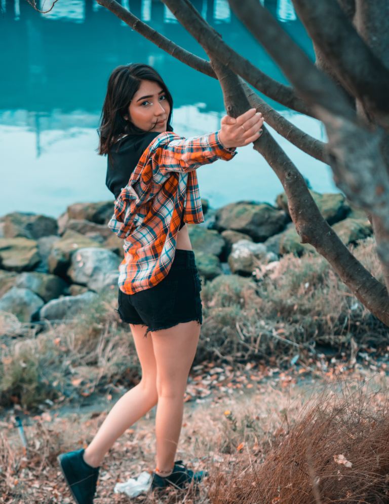 woman wearing orange plaid blouse standing beside tree near body of water