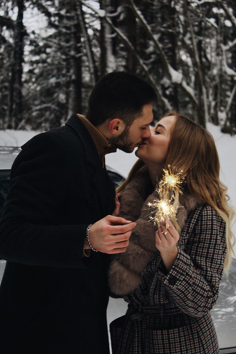 man and woman kissing while holding fireworks