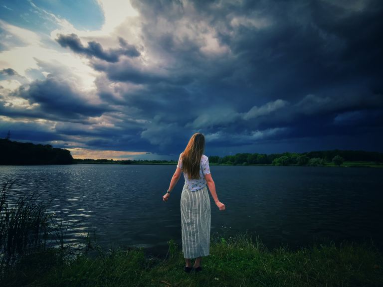 woman in black and white stripe dress standing on green grass field near body of water