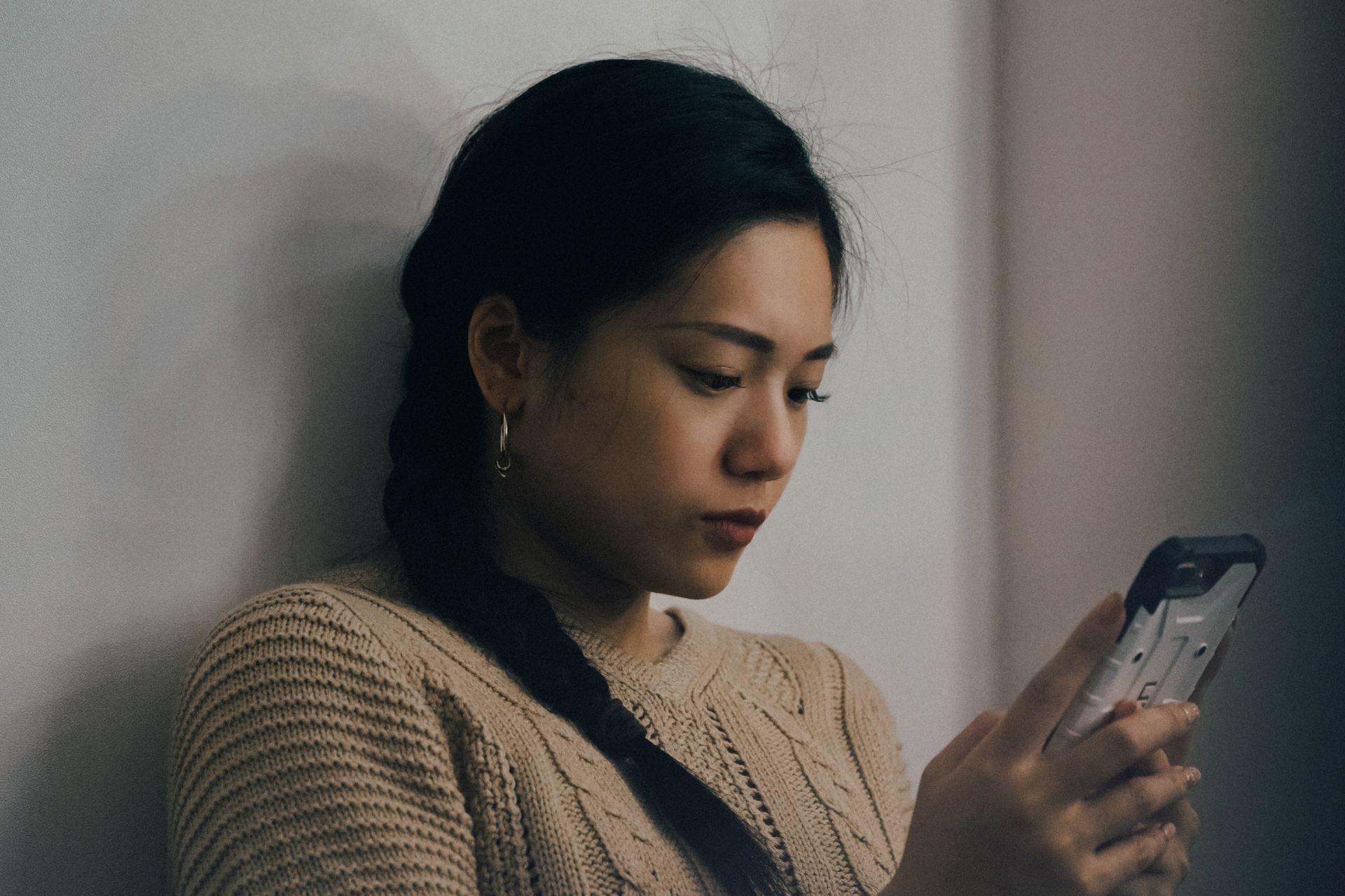 woman leaning back on white wall and using smartphone