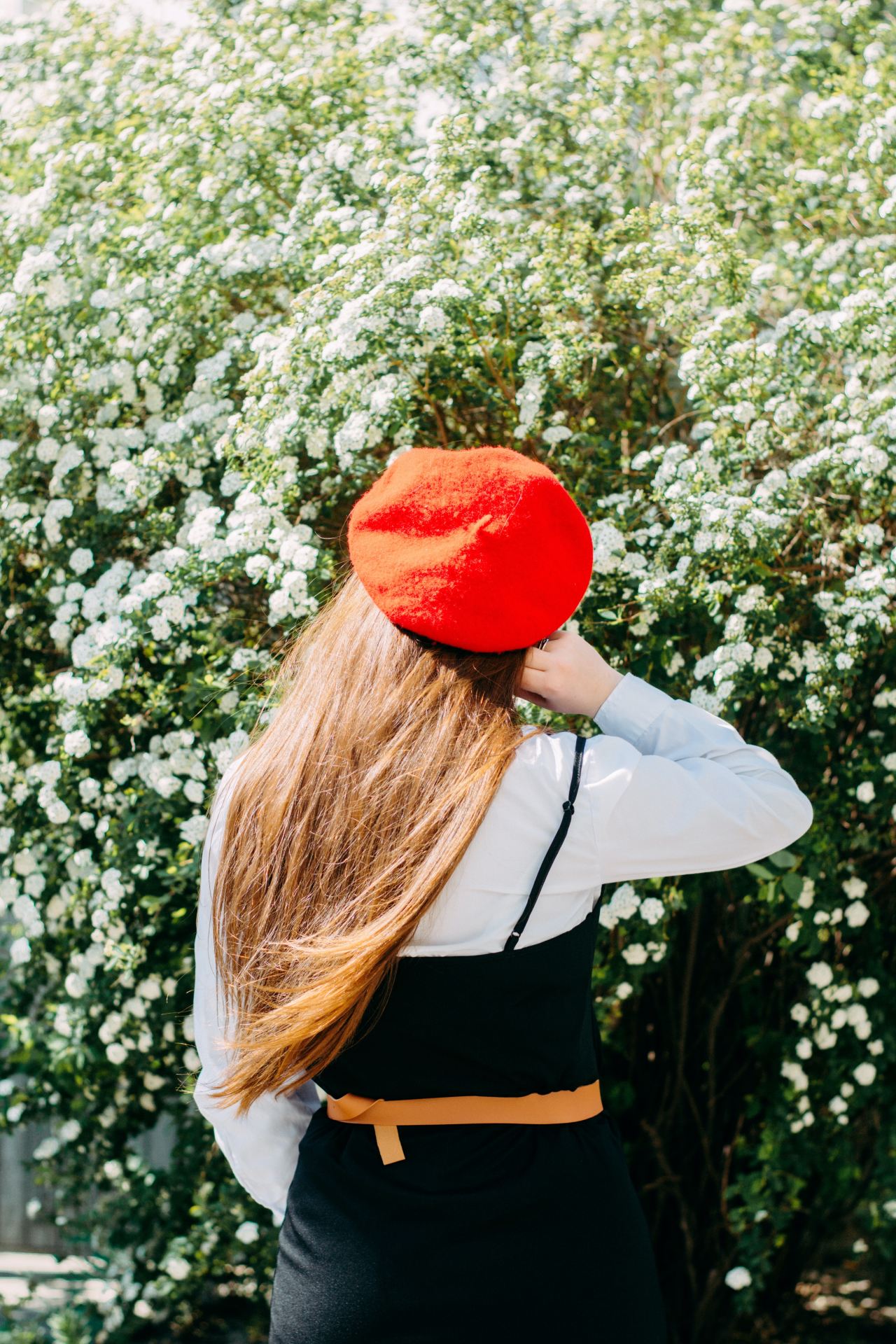 woman in white long sleeve shirt and red hat standing near white flowers during daytime