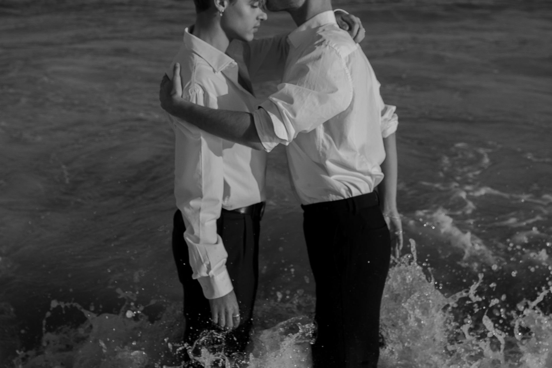 grayscale photo of two man standing on body of water