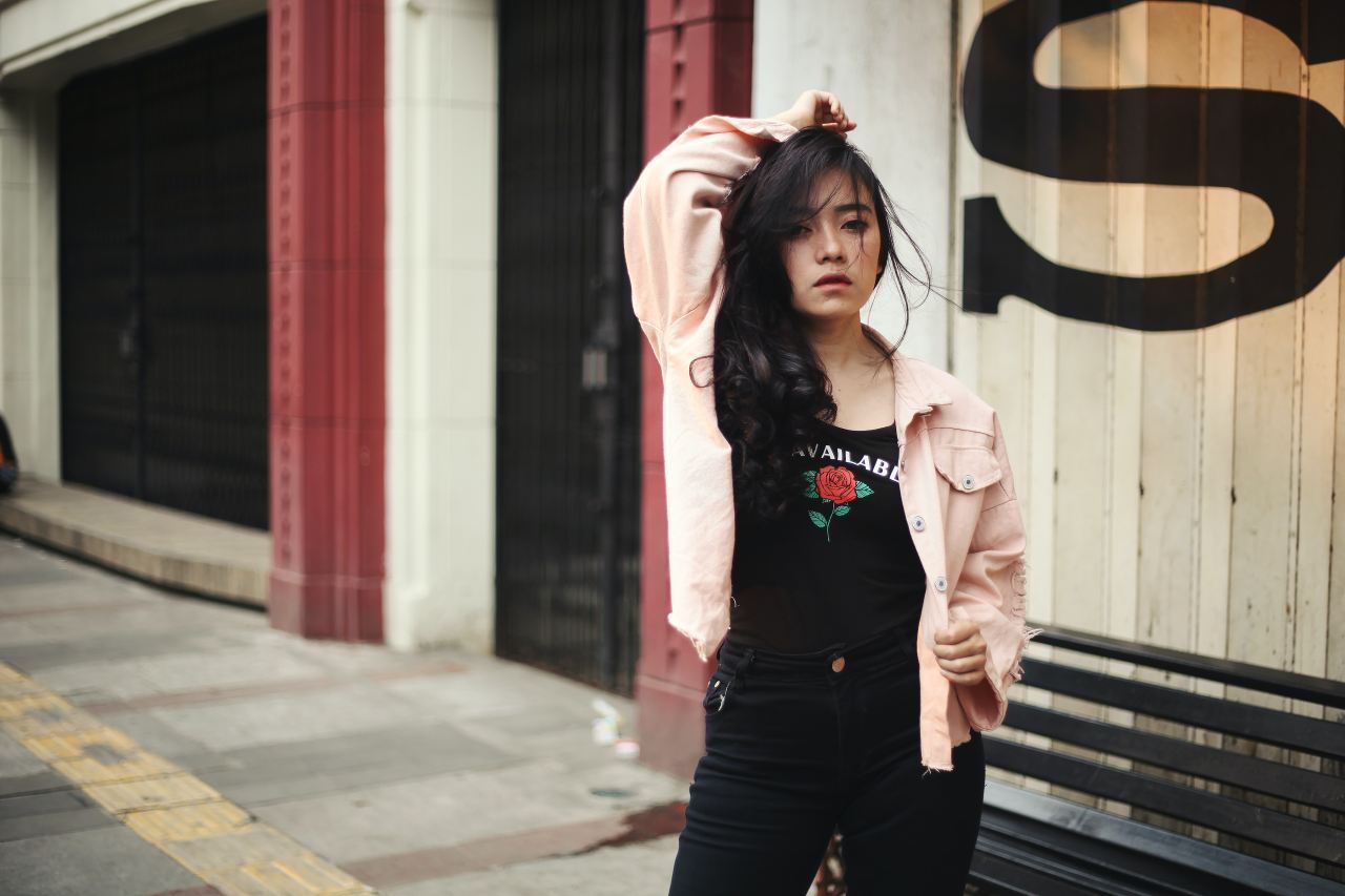 woman in pink long sleeve shirt and black denim jeans standing near white and brown concrete