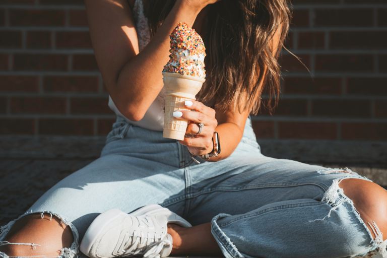 woman in white tank top and blue denim jeans holding white disposable cup