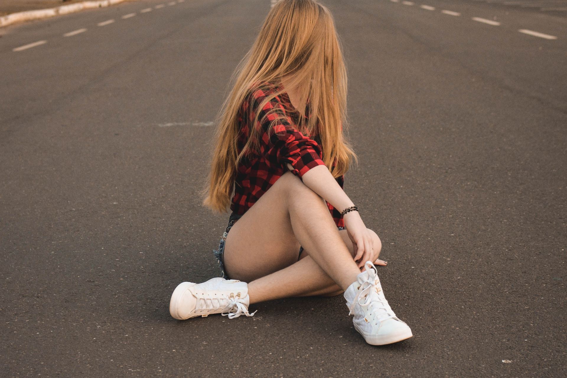 woman in black and red gingham dress shirt sitting on road during daytime