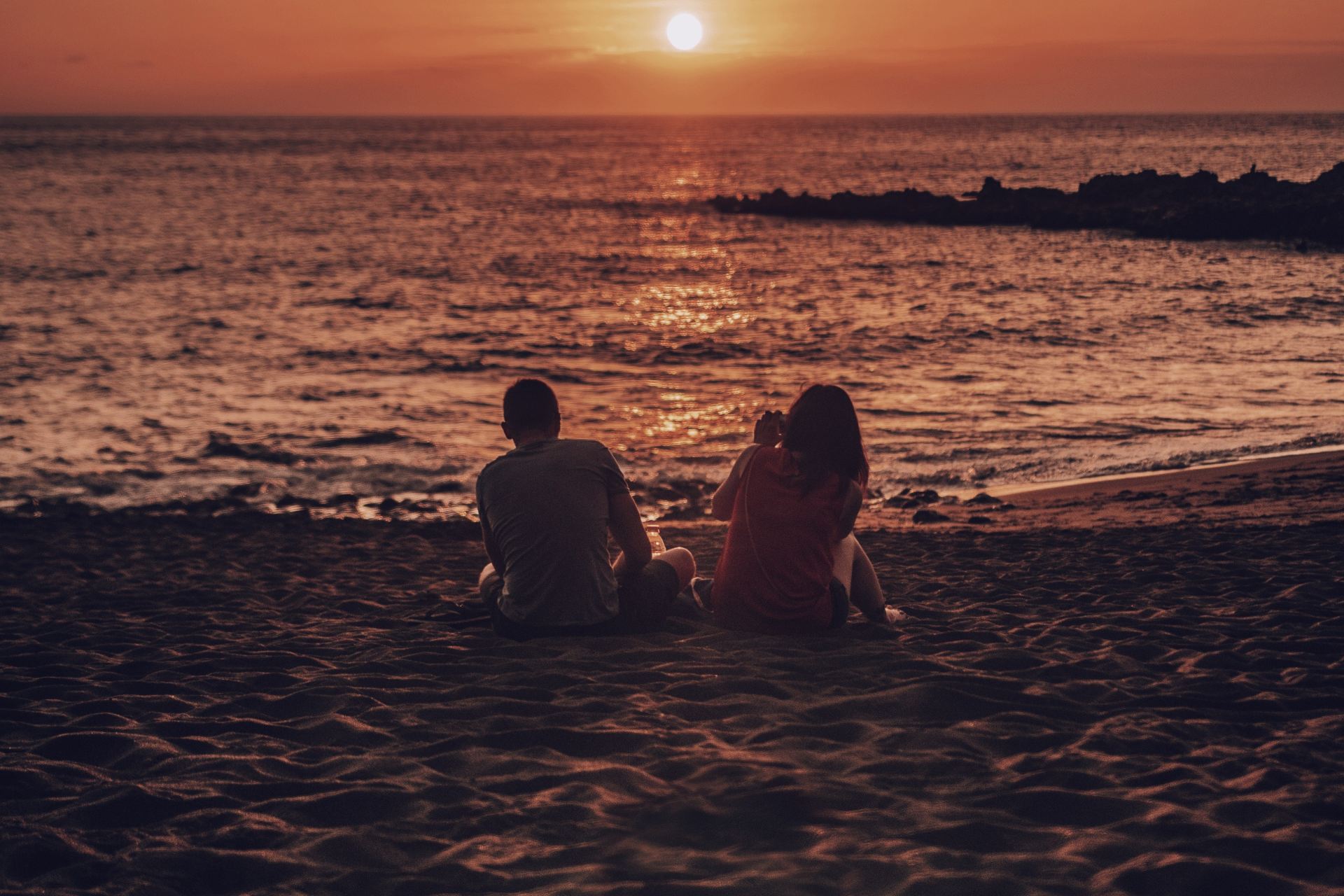 man and woman sitting on beach during golden hour