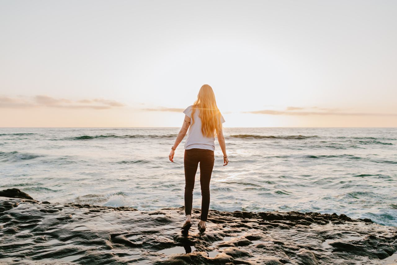 woman in white long sleeve shirt and black shorts standing on beach shore during daytime