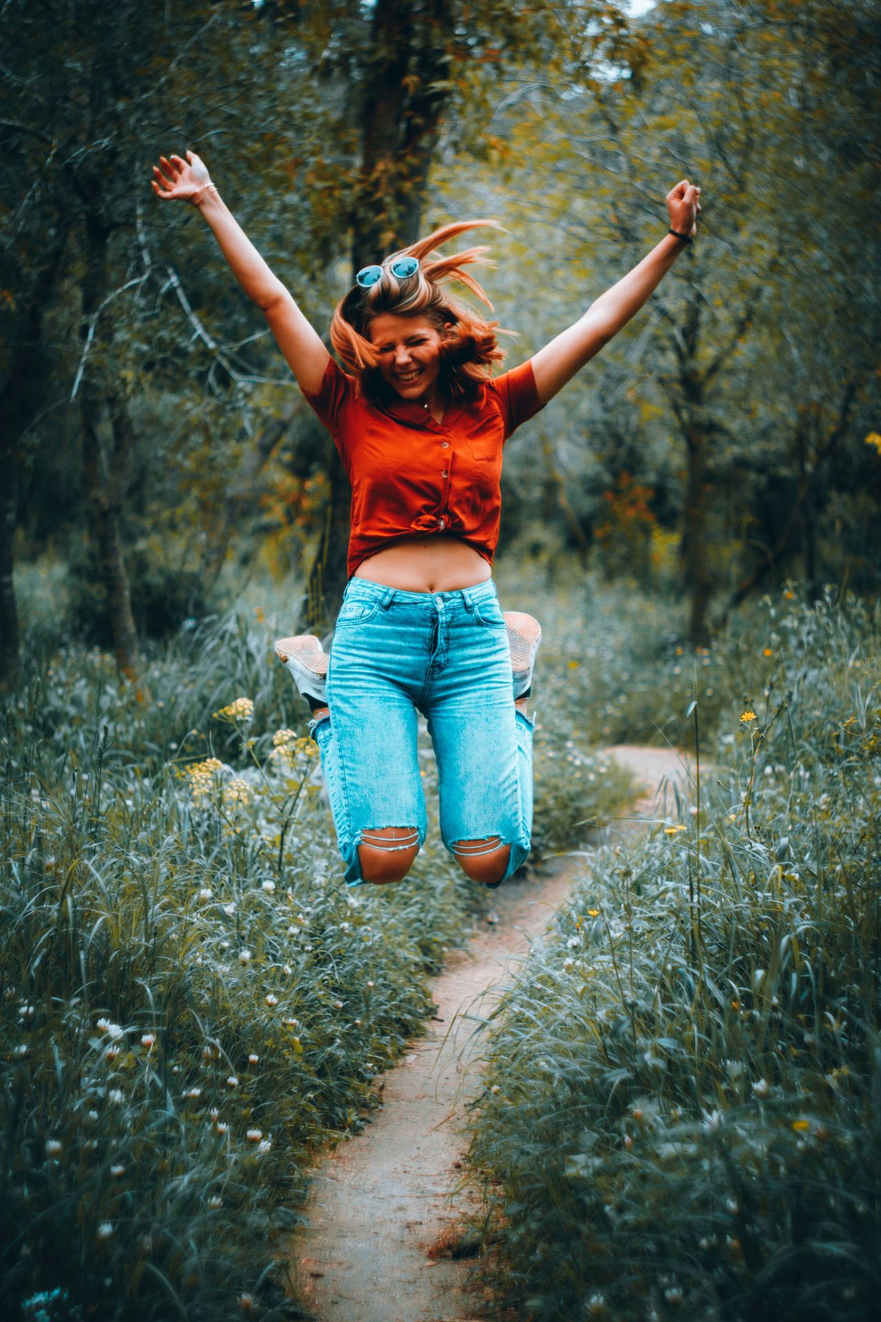 woman in orange t-shirt and blue denim jeans standing on green grass field during daytime