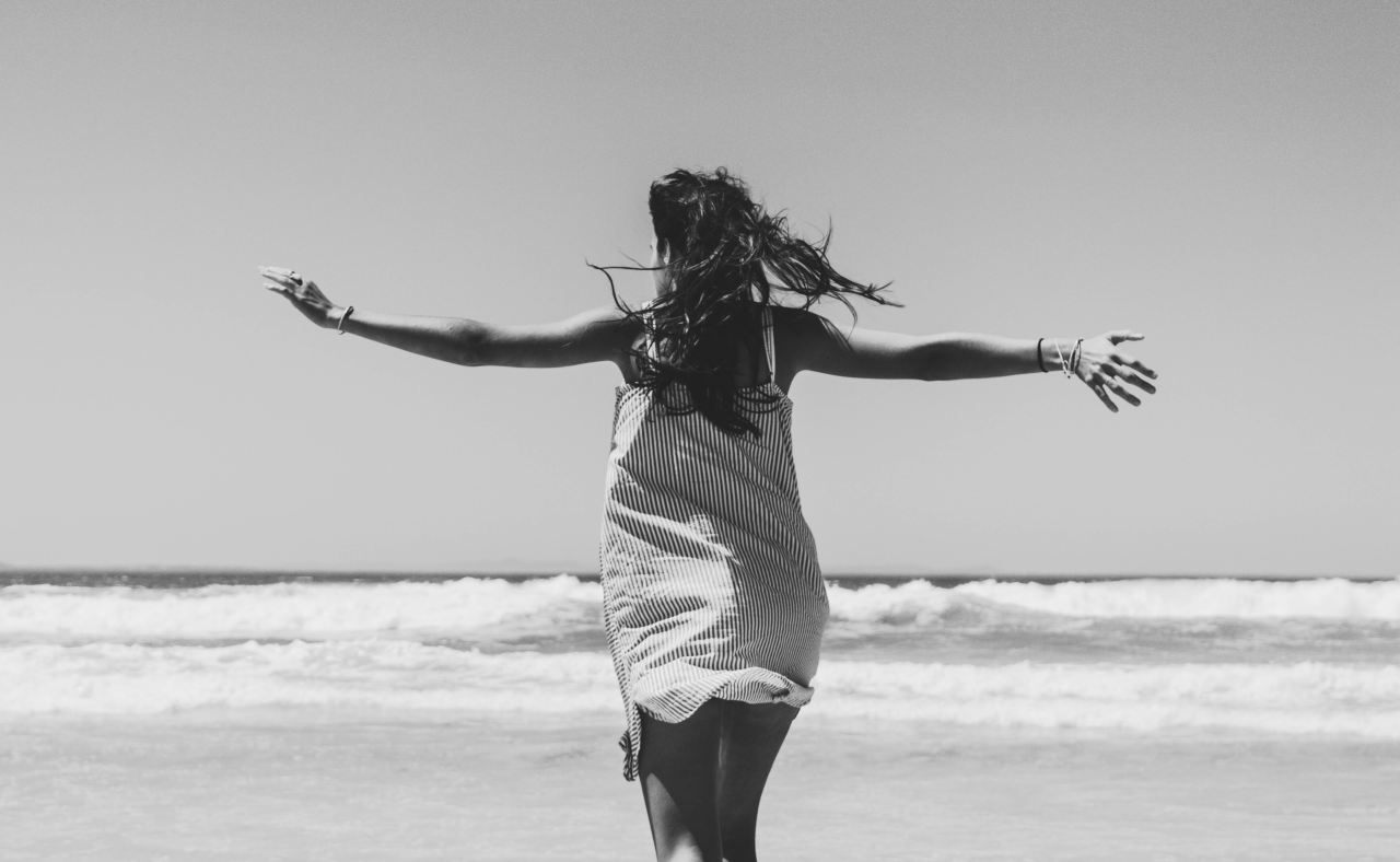 woman standing facing beach with arms wide open