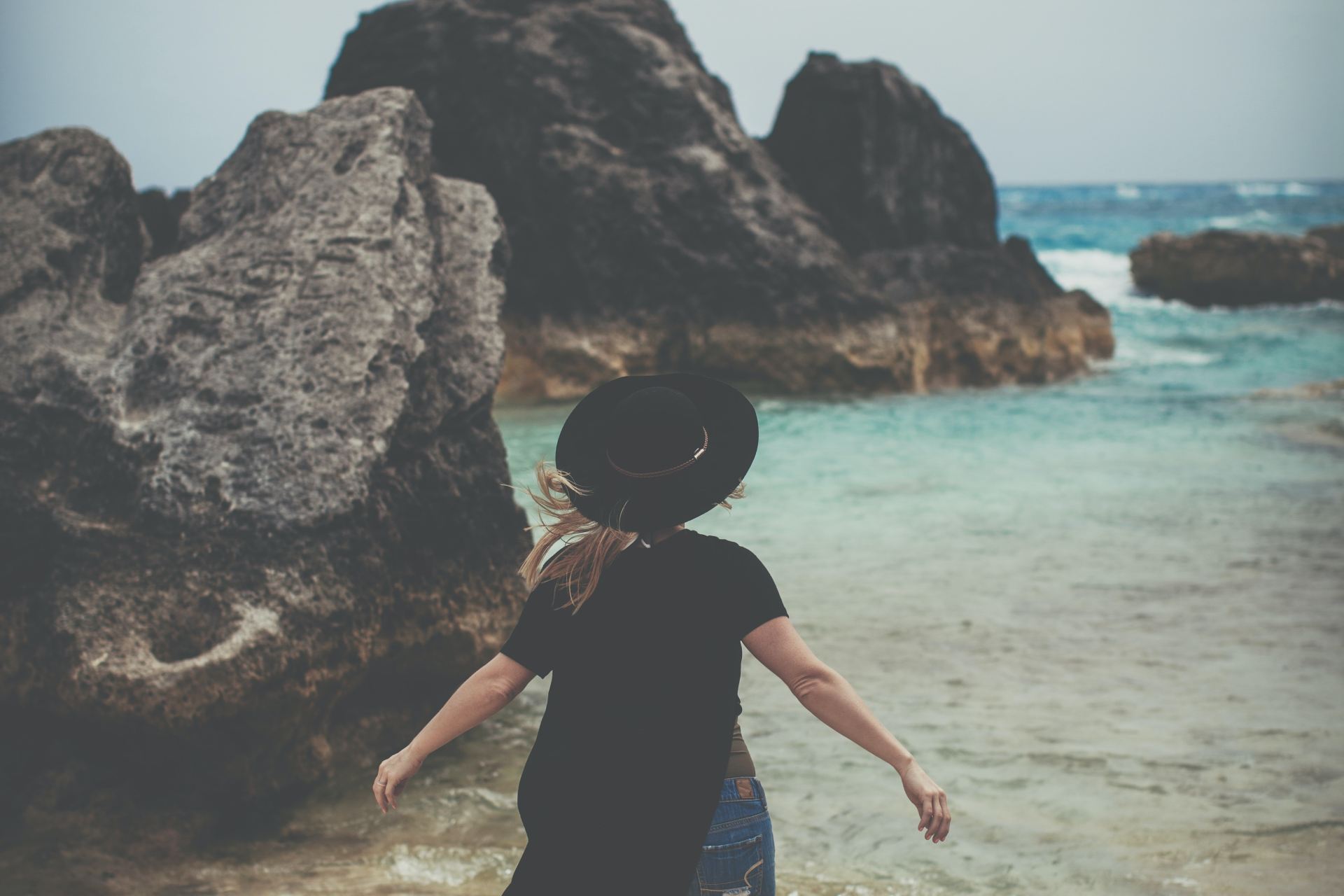 woman standing on rock near ocean shoreline