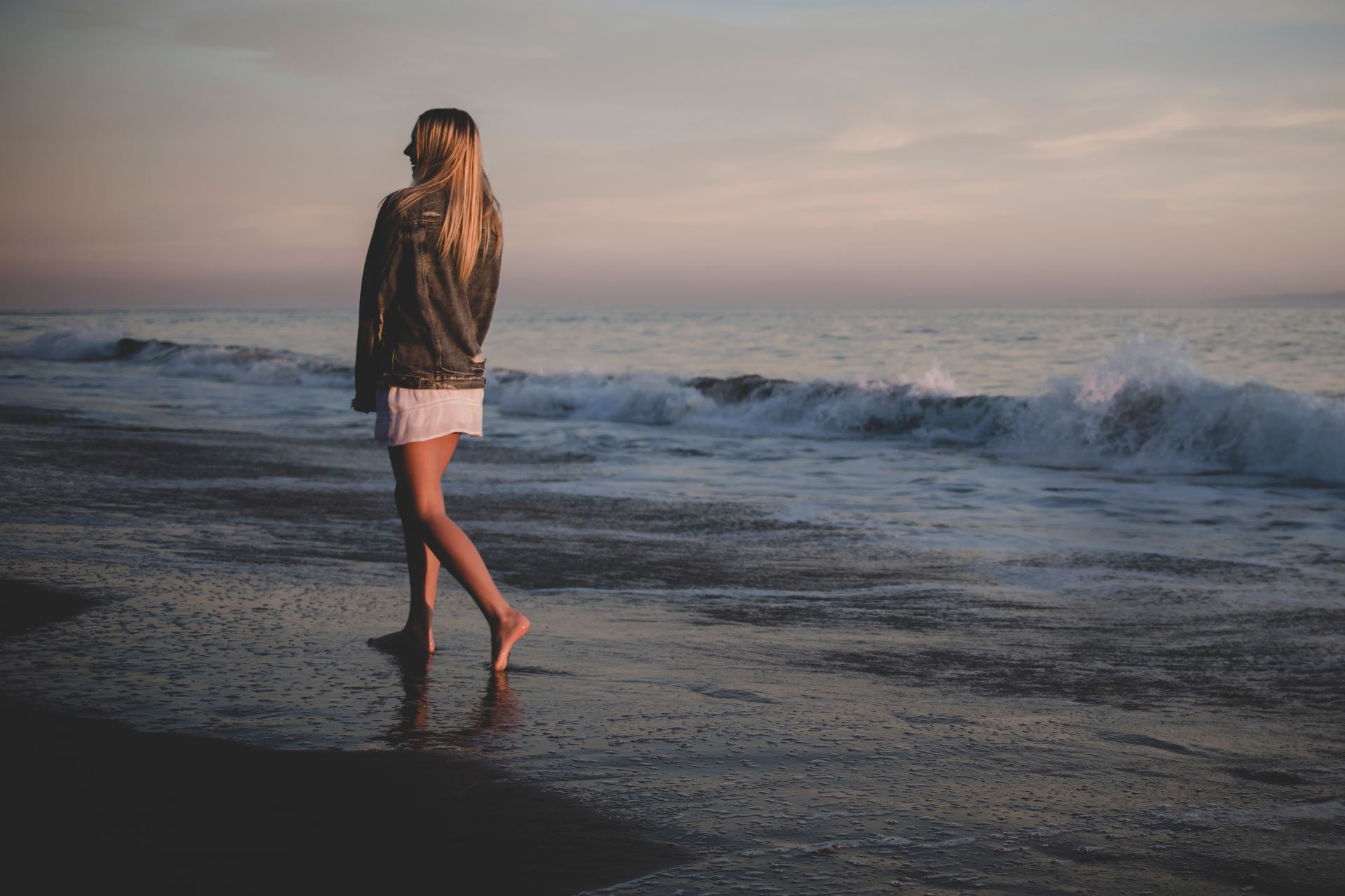 woman walking on seashore under gray sky