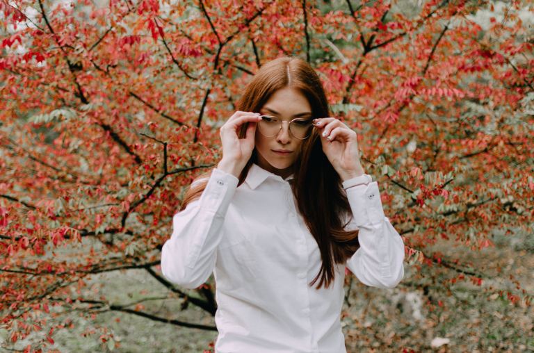 woman in white dress shirt wearing eyeglasses standing near red leaf tree during daytime