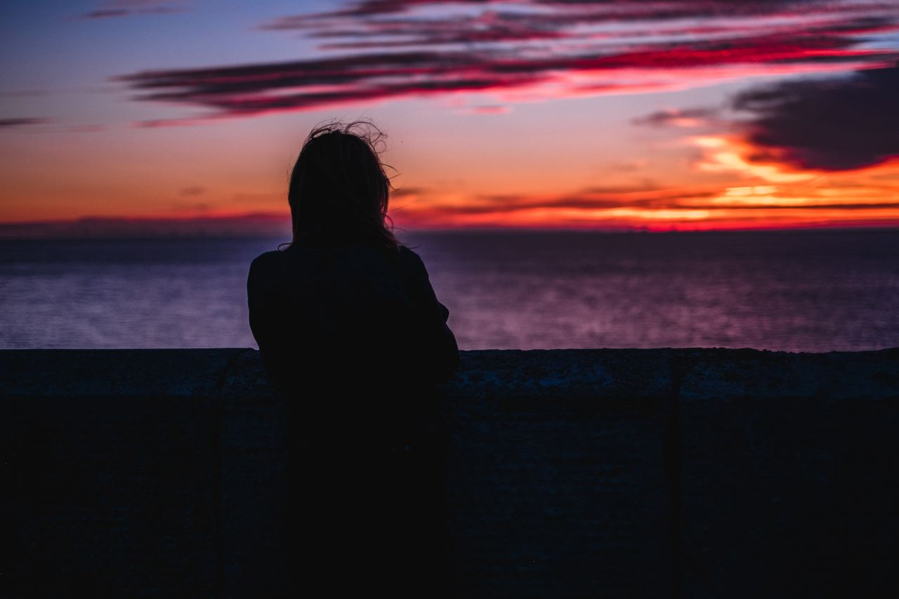 silhouette photo of person standing while looking at the ocean during golden hour