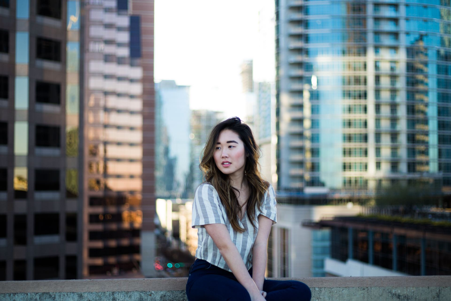 selective focus photography of woman in gray shirt sitting near building edge