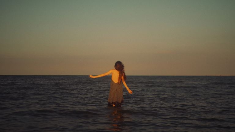 woman in black dress standing on water during sunset