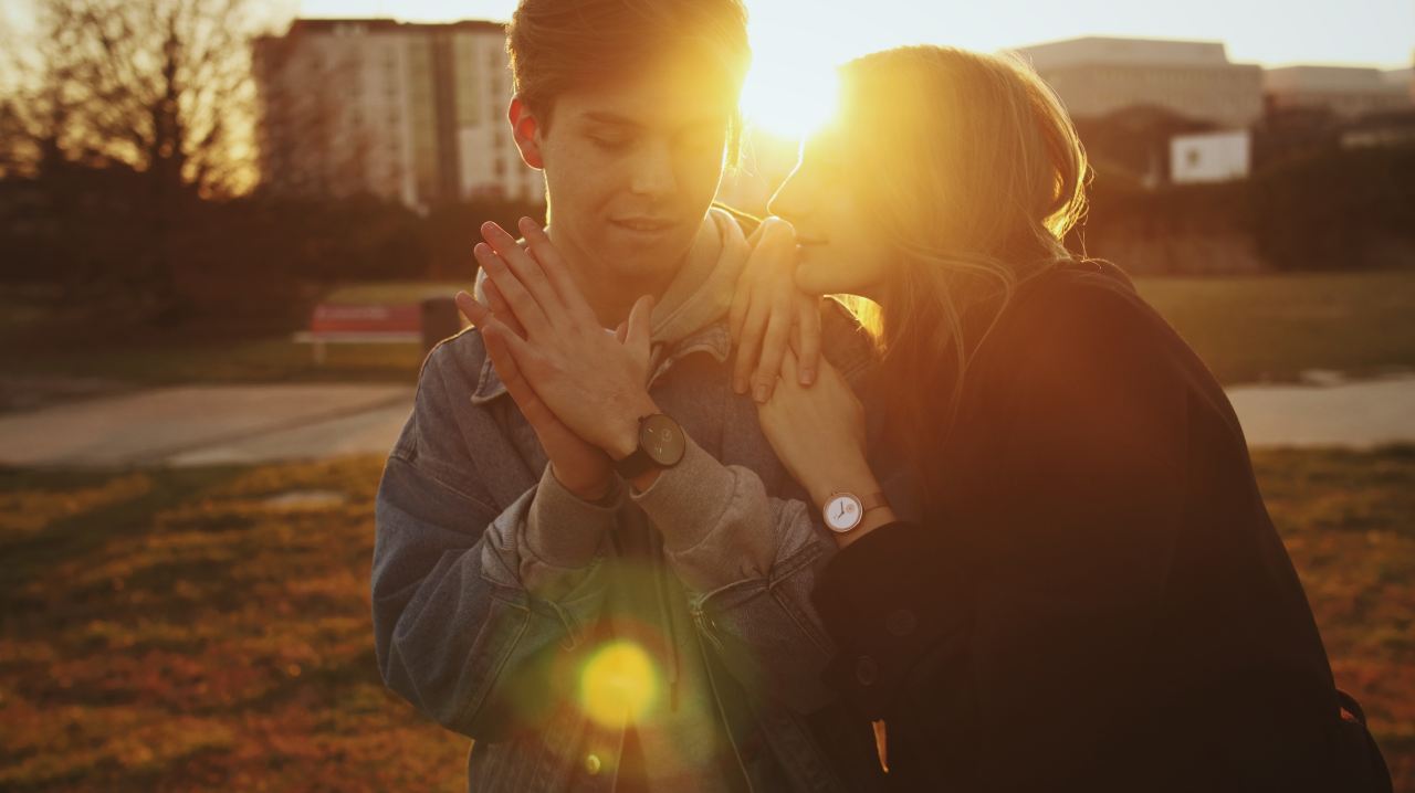 man in black jacket kissing woman in gray jacket during sunset