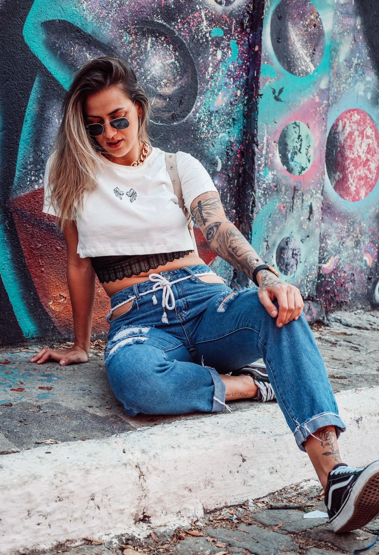 woman in white long sleeve shirt and blue denim jeans sitting on concrete wall during daytime