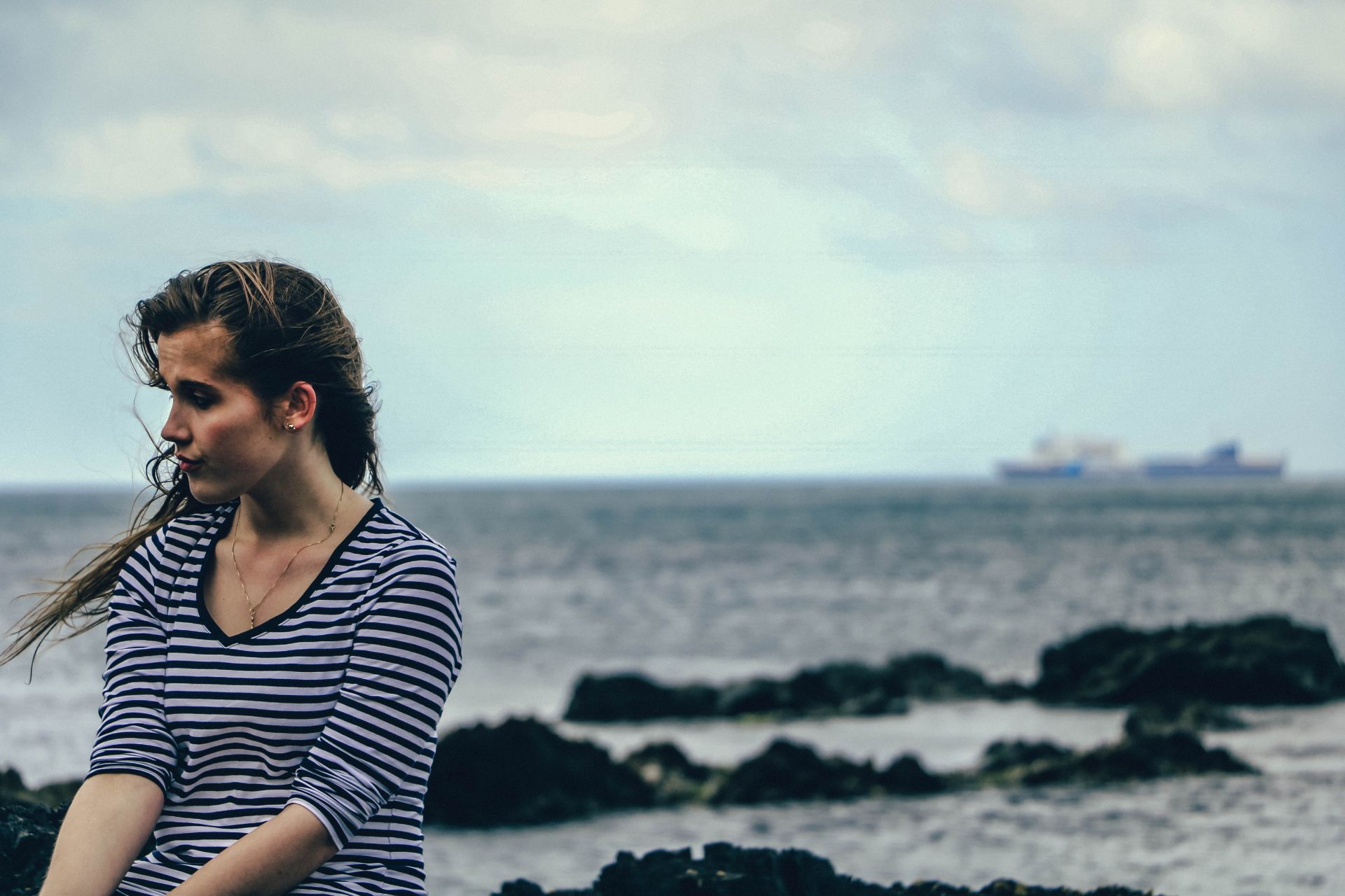 focus photography of woman in black and white striped V-neck elbow-sleeved shirt near sea during daytime